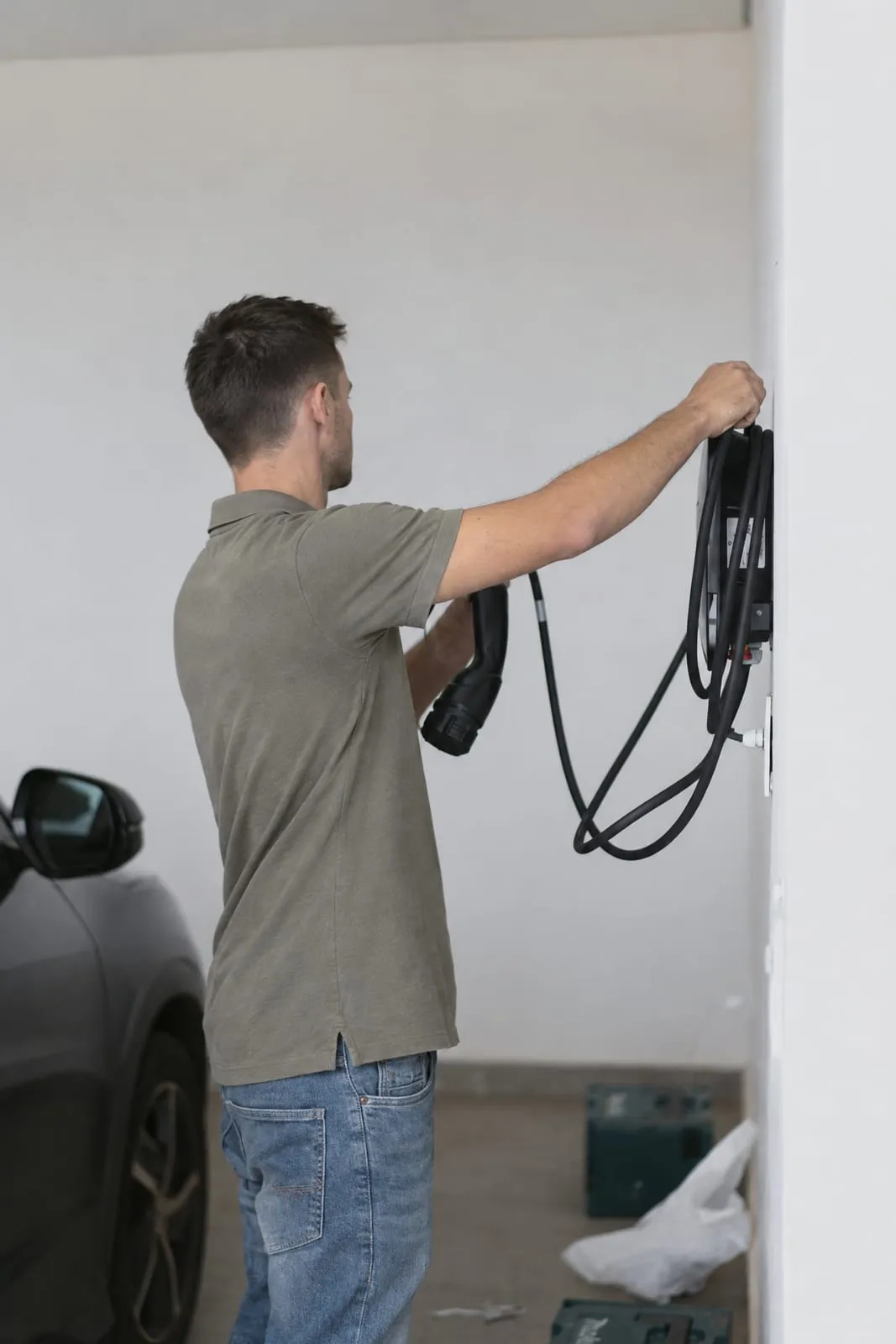 Imagem gerada a partir de foto de obra da Siella: técnico de costas fixando o carregador de veículo elétrico na parede de uma garagem em obra, com o carro ao lado.