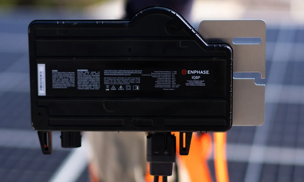 Microinversor Enphase IQ8P instalado em estrutura metálica com sistema solar ao fundo, representando o melhor microinversor para geração fotovoltaica com segurança e eficiência.